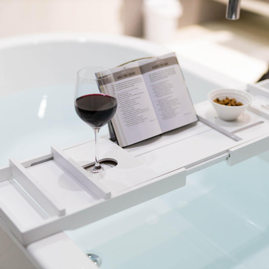 White bamboo bath caddy with glass wine and book on storage platform