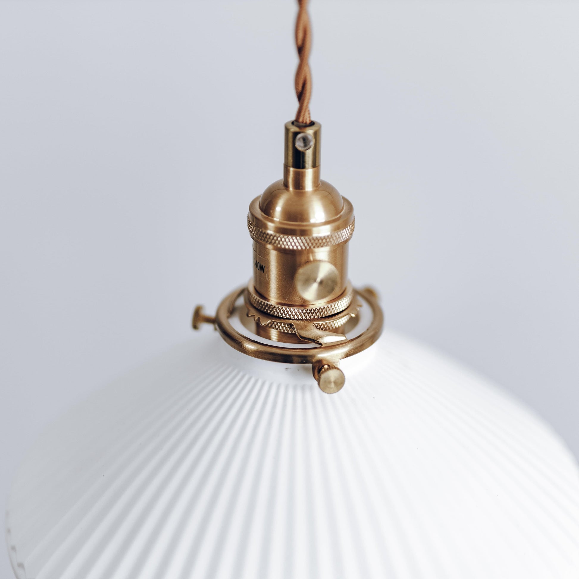 Close view of brass socket and braided cord with white ceramic pleated shade below