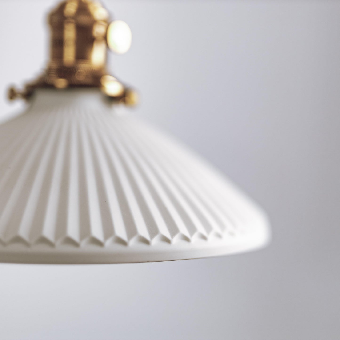 White ceramic pleated pendant shade with brass hardware, hanging from twisted cord