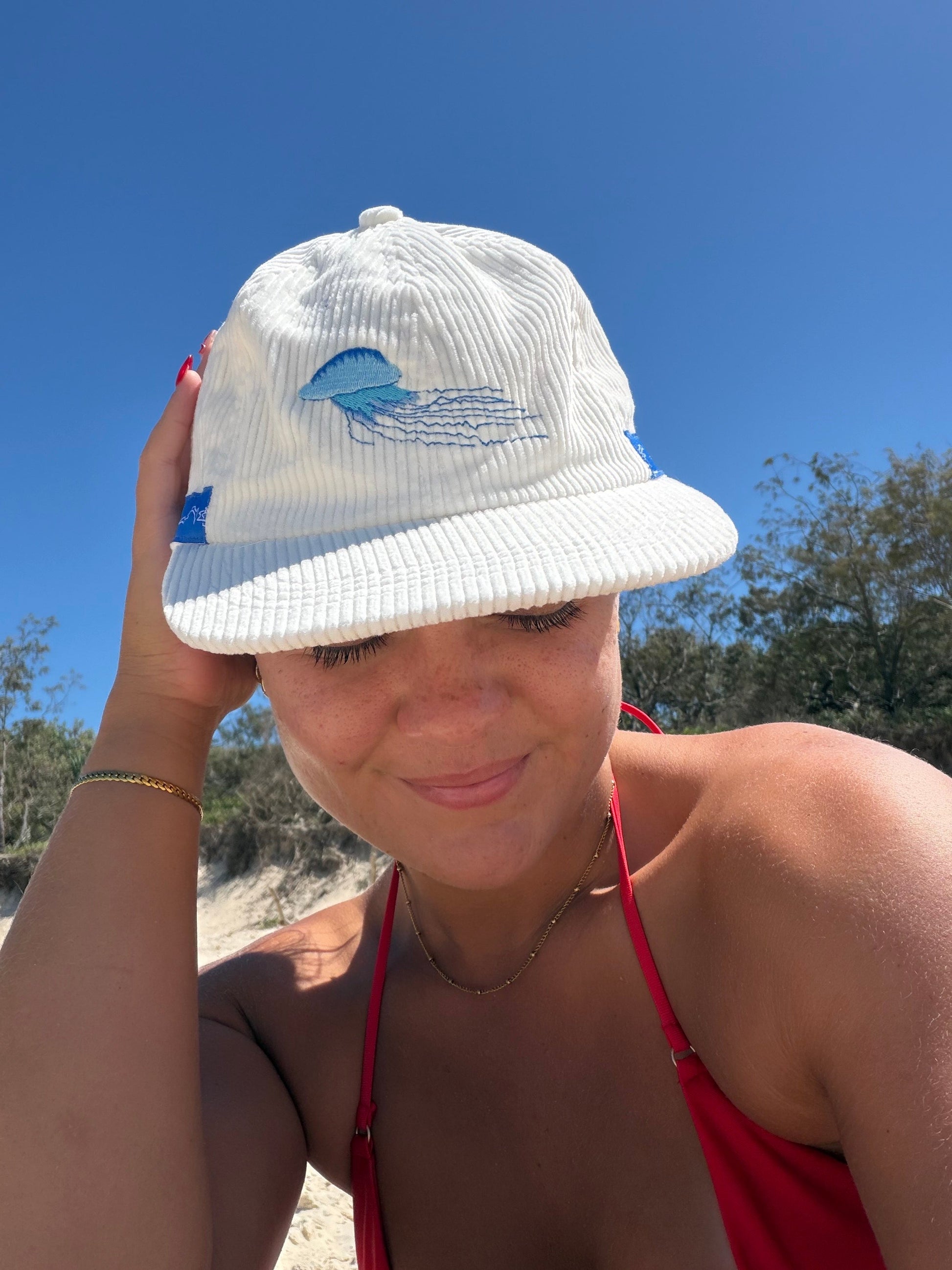 White cap with blue jellyfish embroidery on front panel and blue side band.