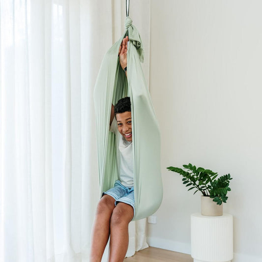 Sage green fabric therapy swing cocoon with overhead rope, person seated inside