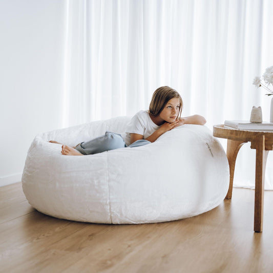 White plush bean bag with person lounging on it, showing the smooth cover