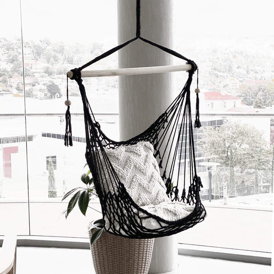 Black macrame hanging hammock chair with open weave seat and white throw pillow