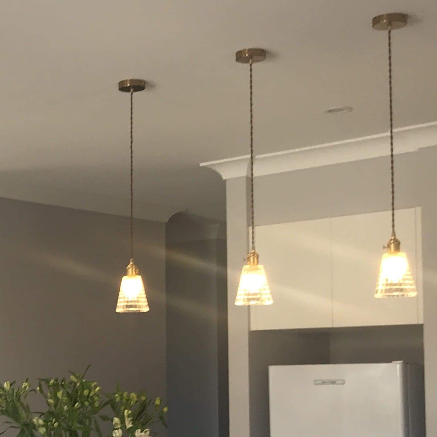 Three clear glass pendant lights with antique brass caps on braided cords.