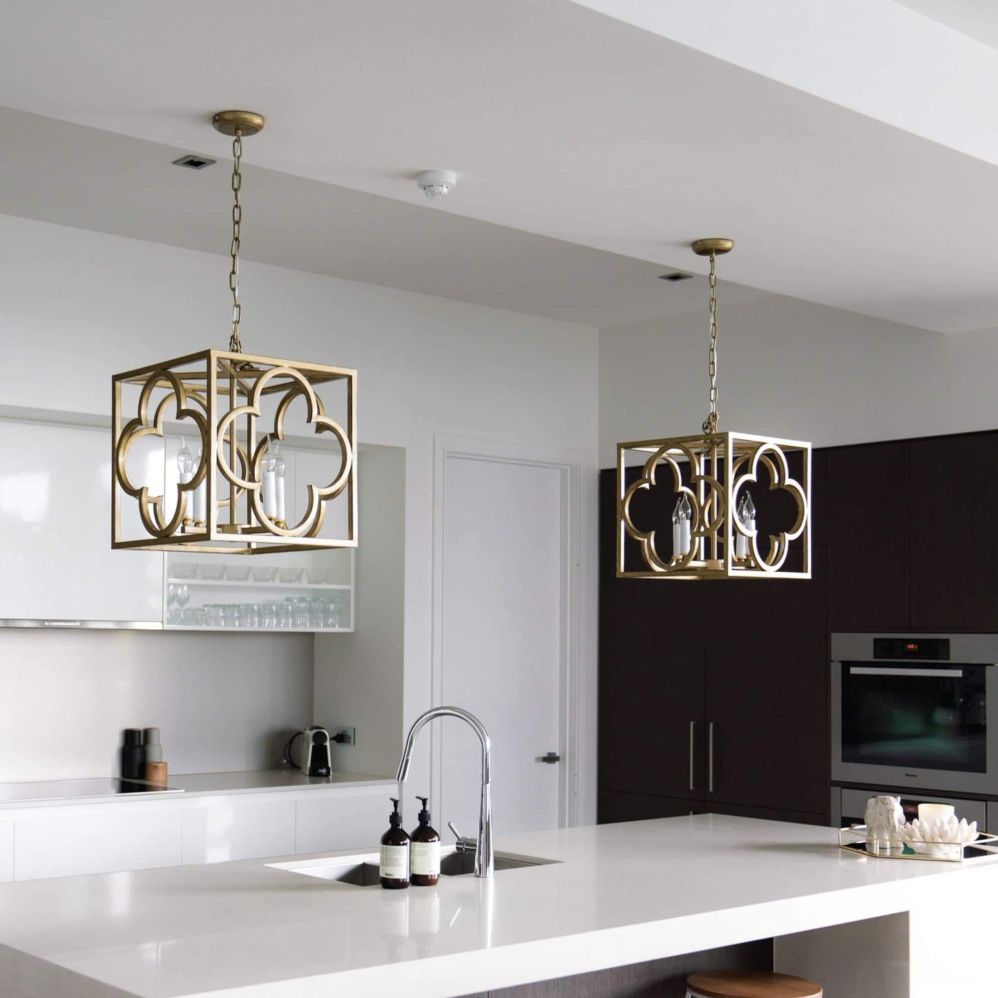 Two gold box frame lantern pendant lights over kitchen island with lit candle bulbs