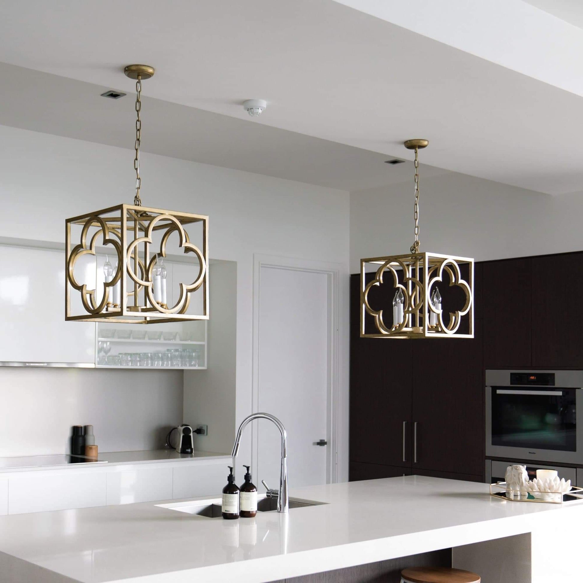 Two gold box frame lantern pendant lights over kitchen island with lit candle bulbs