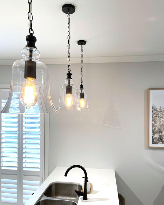 Set of black bell-shape glass pendant lights with metal chains and glowing bulbs in clear shades