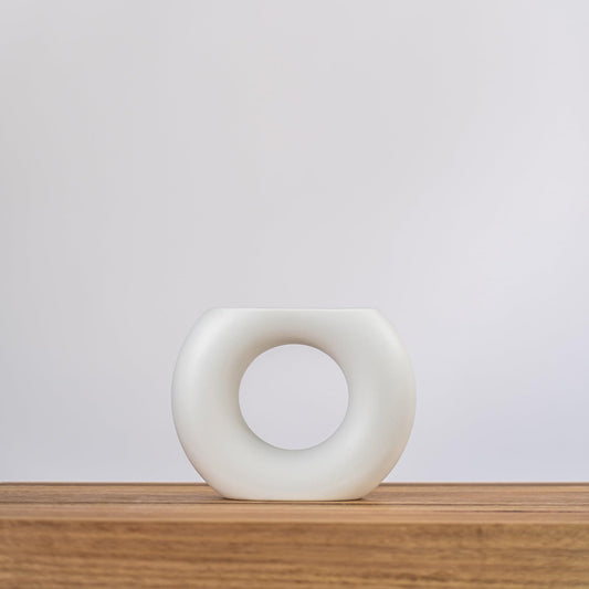 White ceramic vase with circular-oval opening, standing on a wood surface
