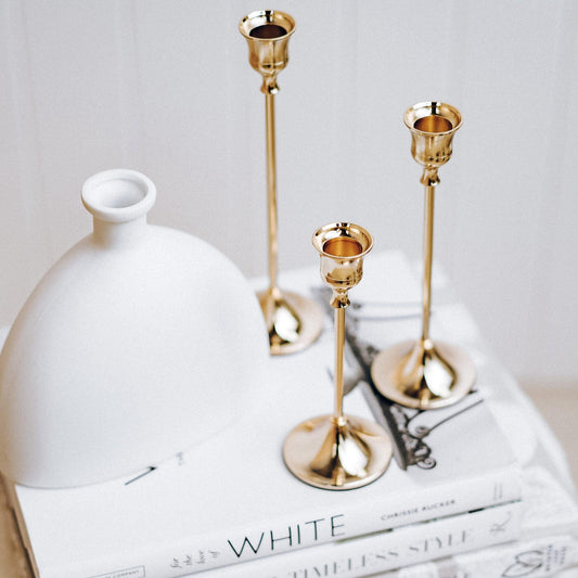 Close-up of 3 rose-gold taper candlesticks with fluted cups and tall stems on display