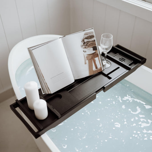 Black bamboo bath caddy with open book, candles, glass, and tray for tub
