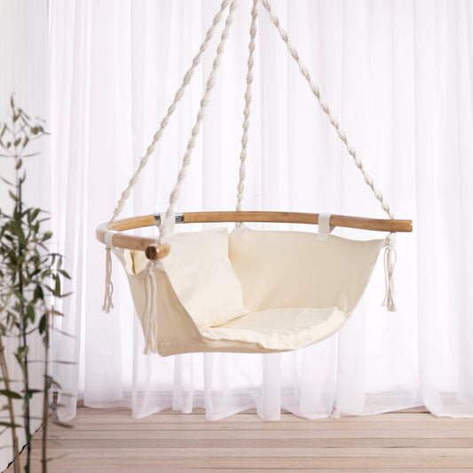 Cream padded hanging hammock chair with wooden bar support and tied rope fringe