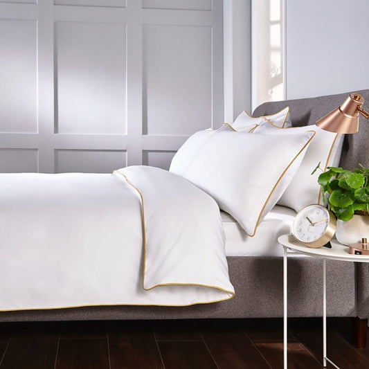 White quilt cover set with gold piping, two matching pillow covers on bed
