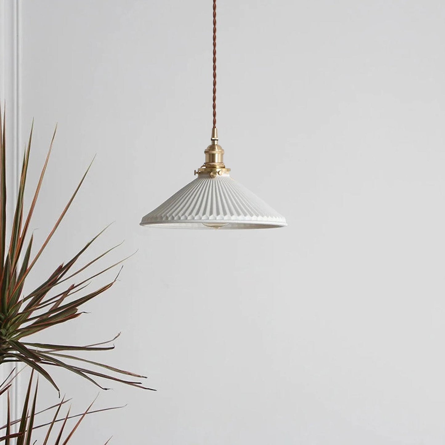 Ceramic pleated pendant light with white ribbed shade and brass cap, suspended on cord