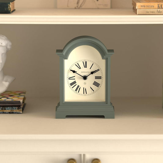 Asparagus green mantel clock on shelf, arched dial with roman numerals and black hands.