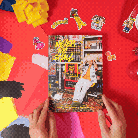 Magazine cover held in hands, “Never Too Small” headline on a red background with stickers