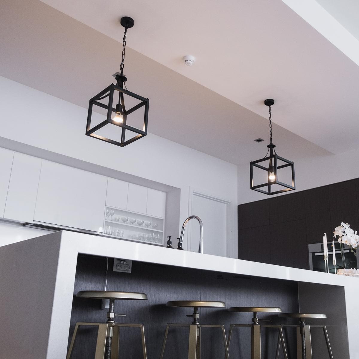 Black lantern pendant light with open metal cage and visible warm bulb