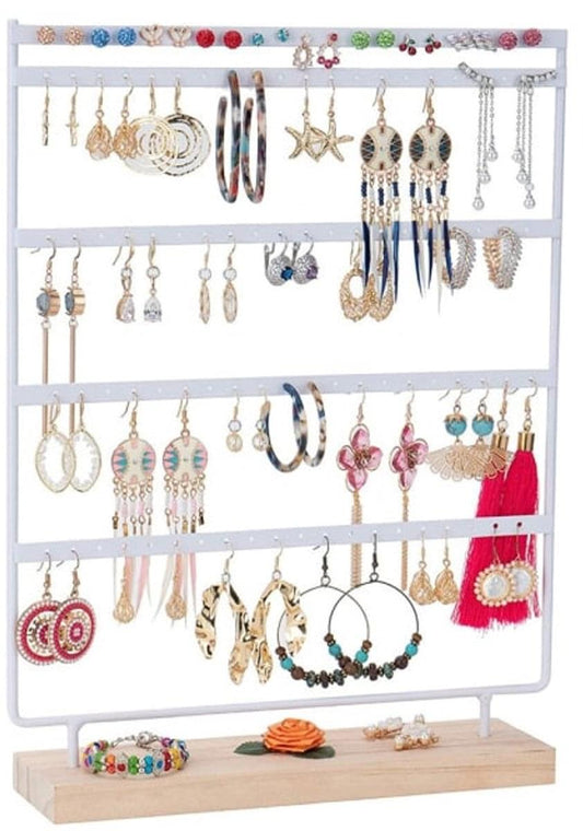 White jewelry stand with 4 tiers and peg holes, holding assorted earrings, bracelets, necklaces