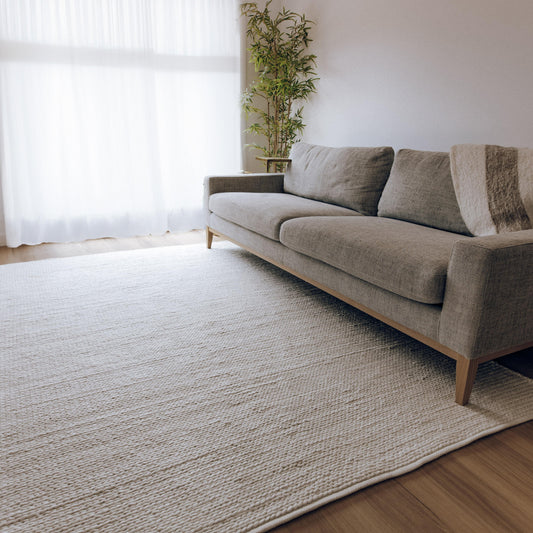 White tones handwoven floor rug under a sofa, showing flat braided texture
