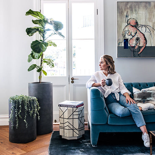 Two dark grey cylindrical plant pots with green plants in a living room setting.