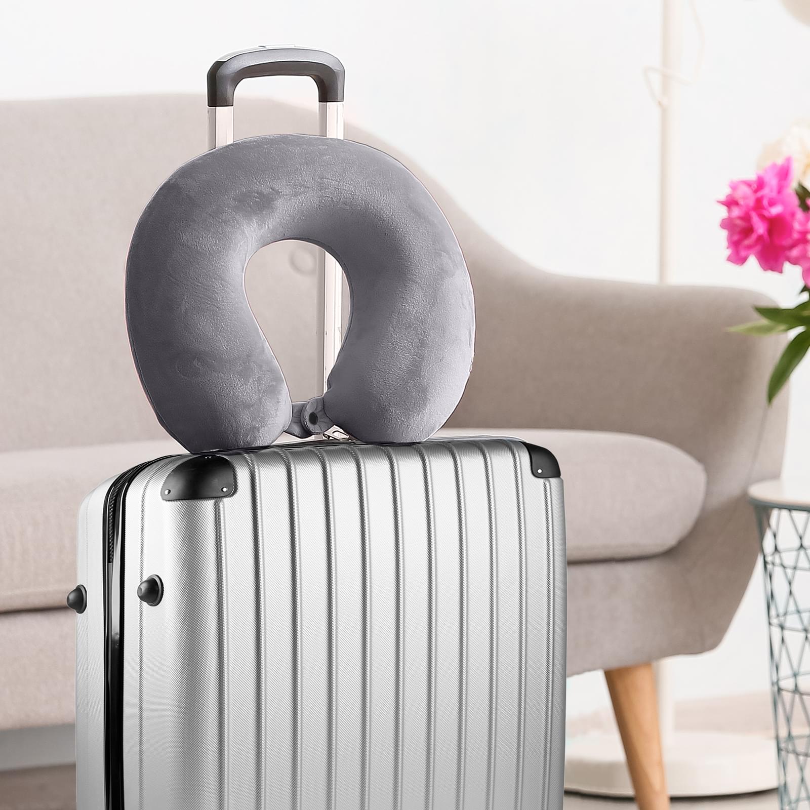 Grey travel neck pillow with clip attachment standing on top of a suitcase