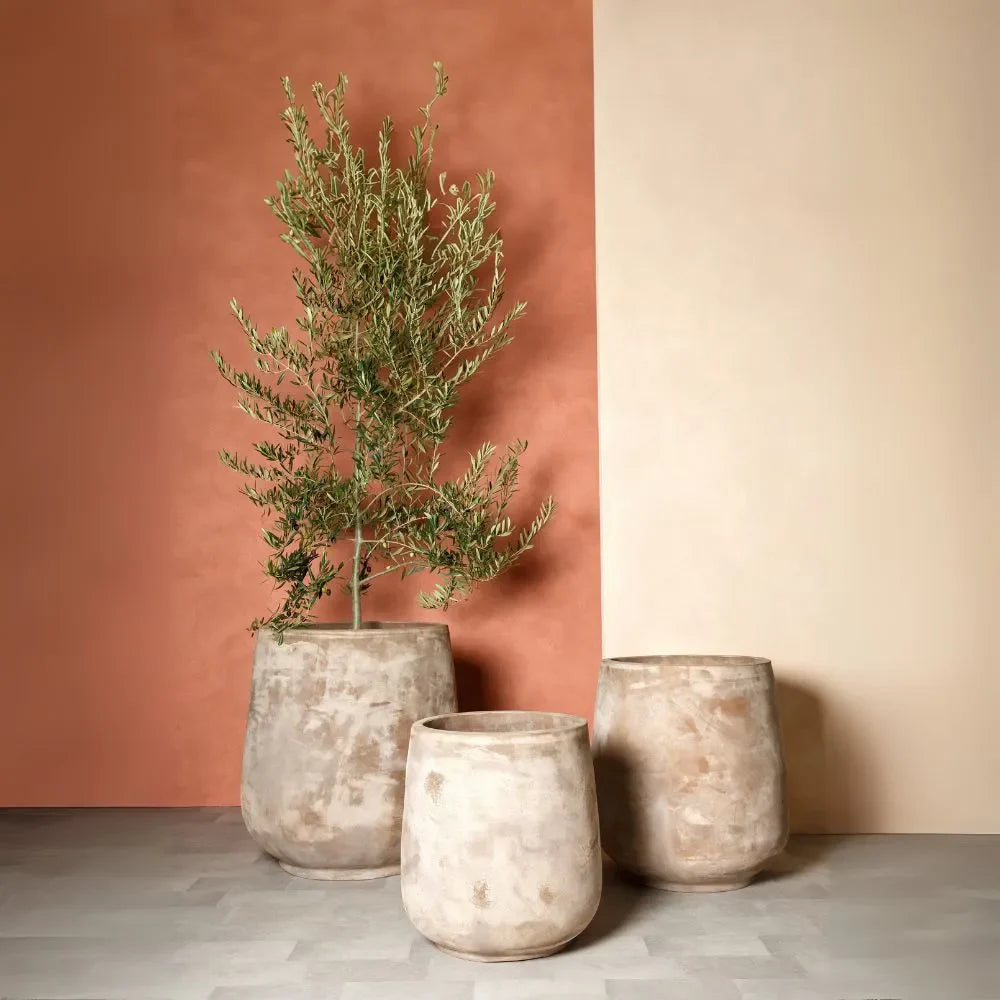 Set of three beige stone-look planter urns with open tops, styled with dried branches