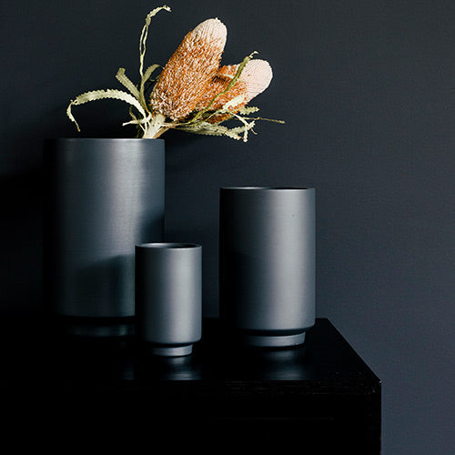 Dark charcoal cylindrical planter set with three pots and a textured leaf arrangement.