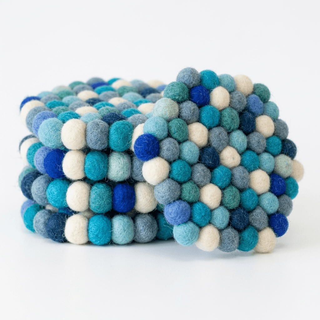 Round wool felt coaster with dense pom-pom surface in ocean blue, green, and cream
