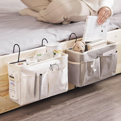 White bedside storage organizer with multiple compartments and top loop handles on bed