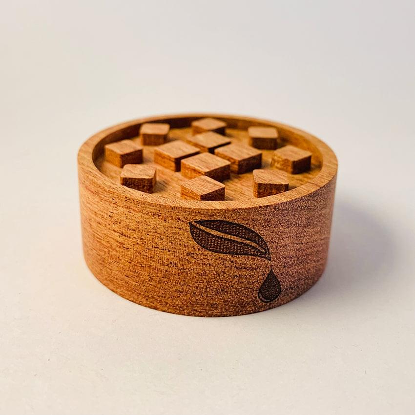 Round wooden diffuser with square cutouts on top and leaf-like emblem