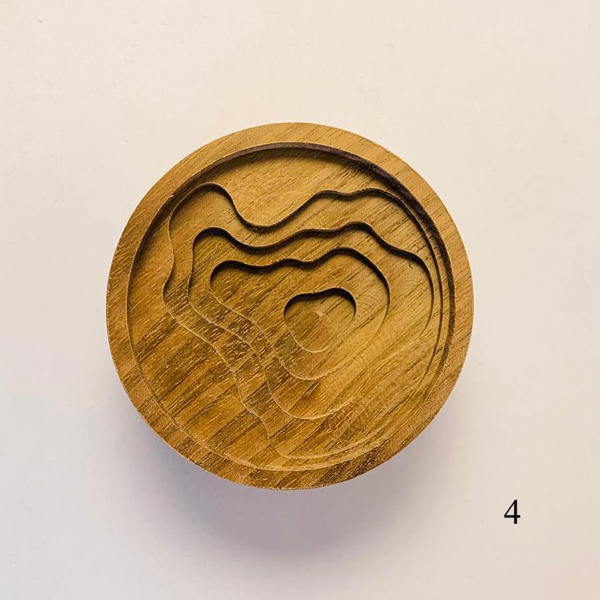 Round wooden diffuser lid with carved wavy lines and abstract animal profile