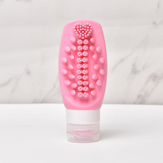 Pink silicone squeeze refill bottle with built-in massage brush and clear refill reservoir