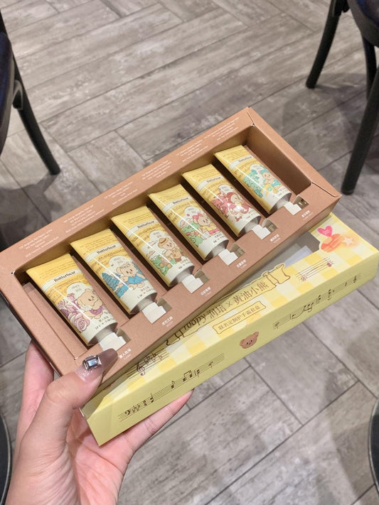 Six mini hand cream tubes in a brown tray within an open gift box, held in hand
