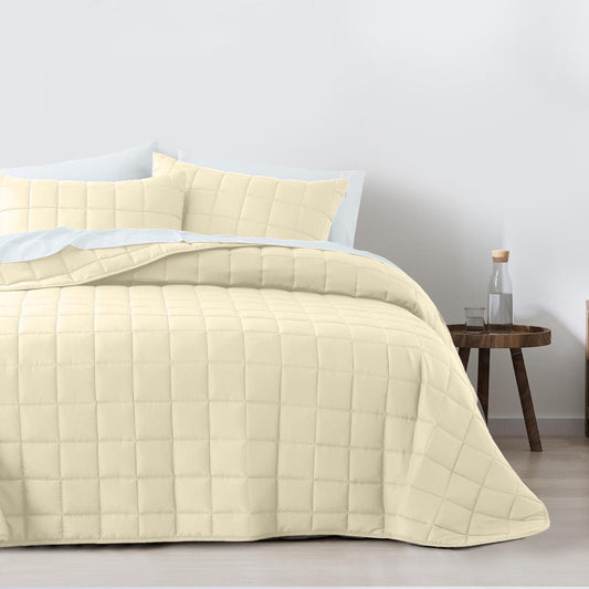 Light beige quilted coverlet and pillow shams set on a bed