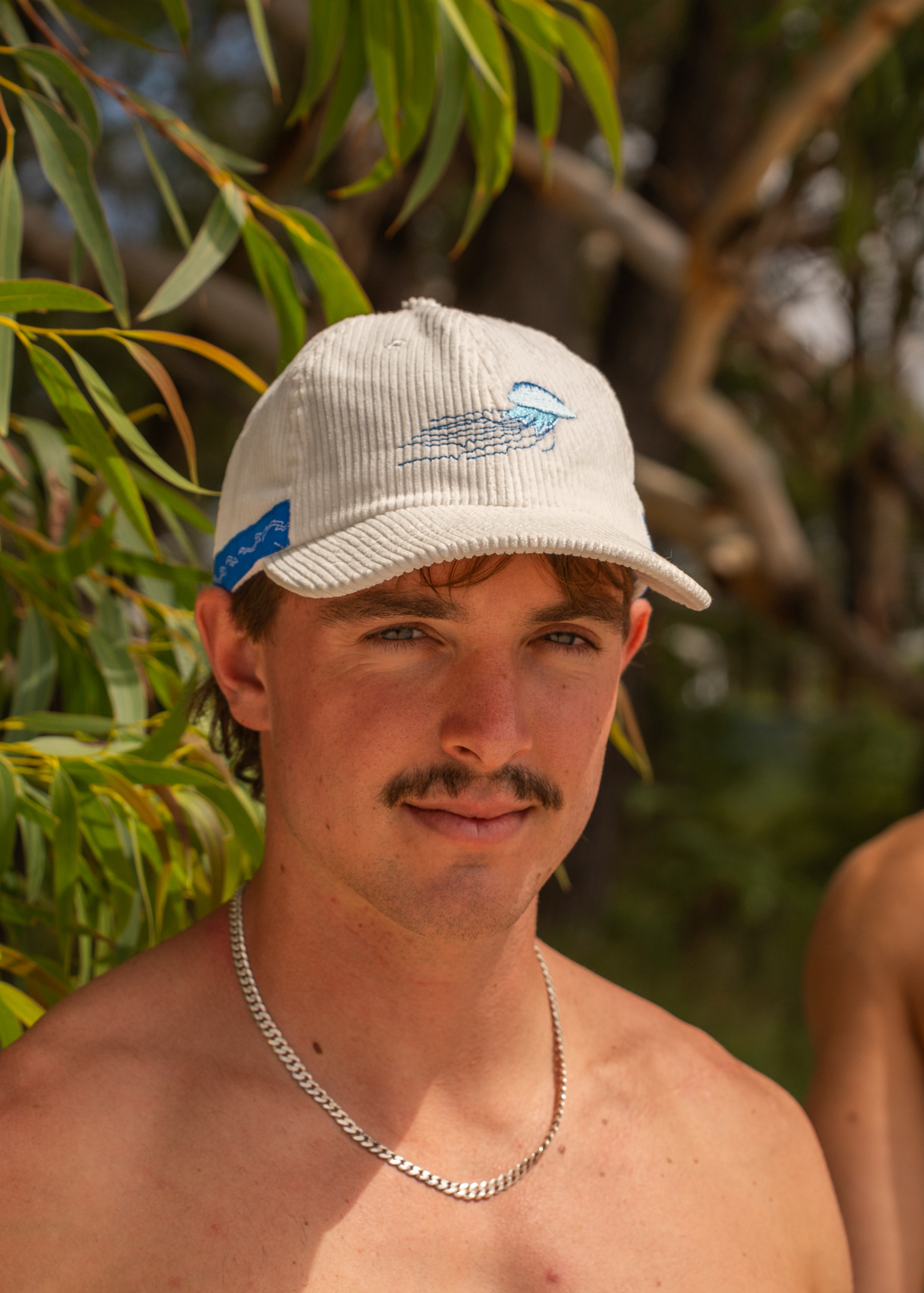 White corded cap with embroidered blue jellyfish and blue side label on brim.