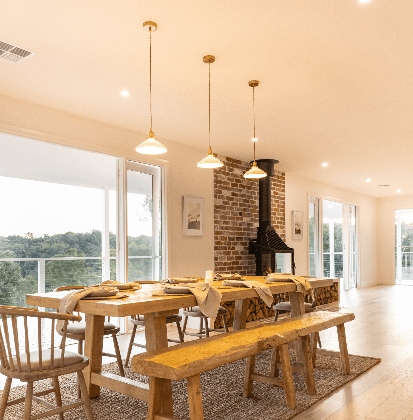 Set of ceramic pleated pendant lights with white shades and brass housings over dining table