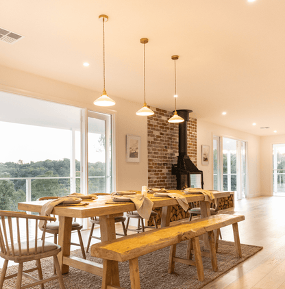 Set of ceramic pleated pendant lights with white shades and brass housings over dining table