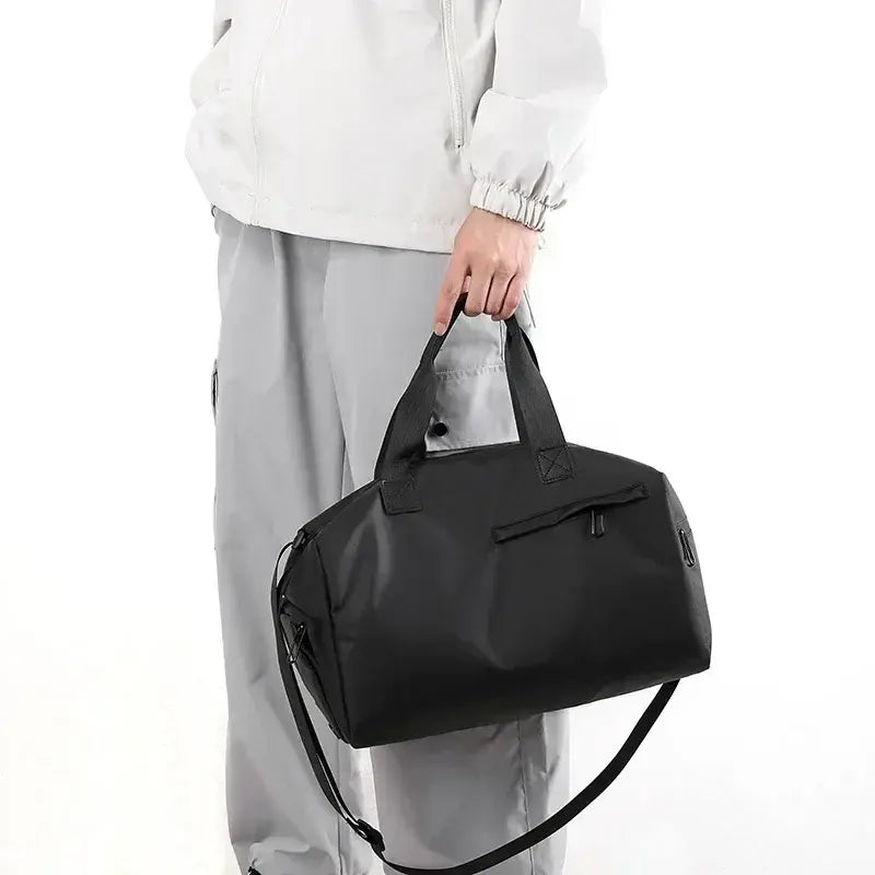 Black duffel gym bag carried by handles with adjustable shoulder strap
