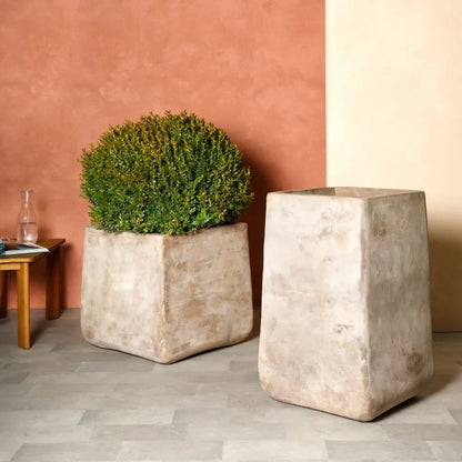 Two beige concrete squircle planter pots with green plants