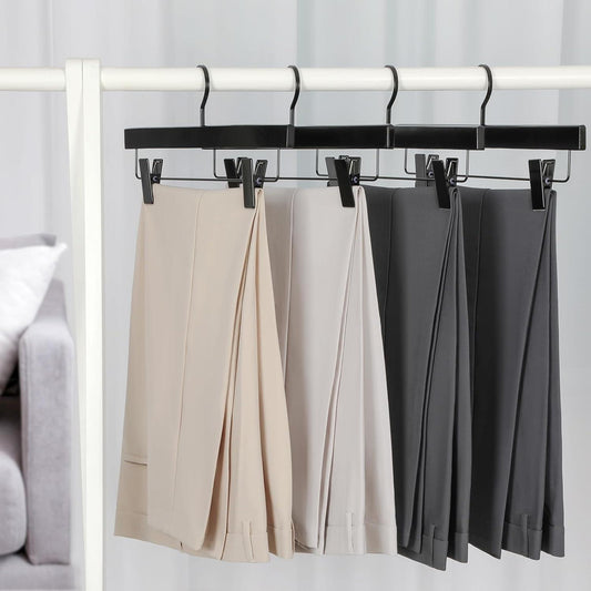 Black pants hangers holding beige and dark trousers on a rod
