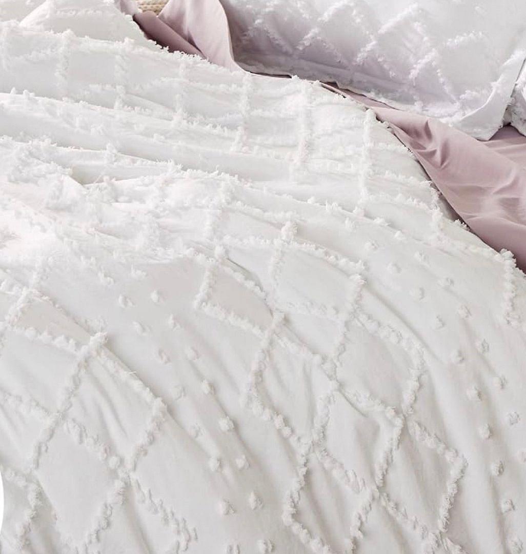White quilt with raised tufted embroidery rows and looped tassel-like accents