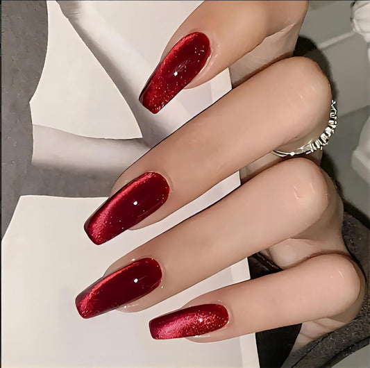 Red coffin-shaped press-on nails with glittery cat-eye sparkle on fingers
