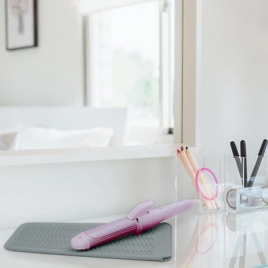 Grey heat-resistant silicone mat holding a pink curling iron on a countertop