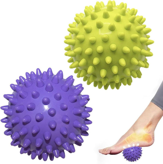 Pair of spiked massage balls, green and purple, with a hand near a foot