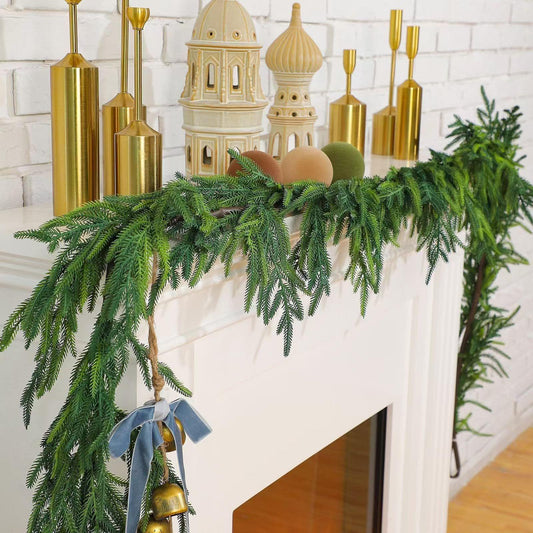 Green artificial pine swag garland with full branches, gold bell and blue bow accents