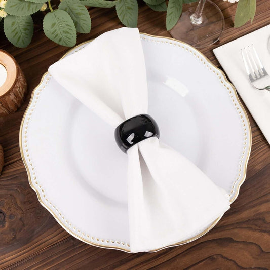 Black acrylic napkin ring holding a folded white napkin on a dinner plate.