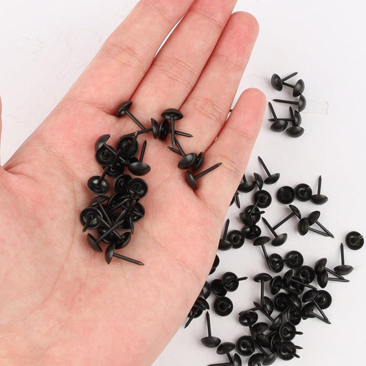 Black thumb tacks scattered on open palm, round heads and pointed tips