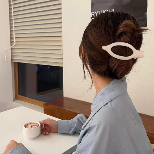 Hair claw clip, cream with oval cutout, holding brown updo bun at back.
