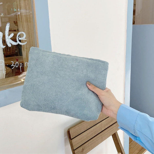 Blue corduroy cosmetic bag with zipper, held in a hand.
