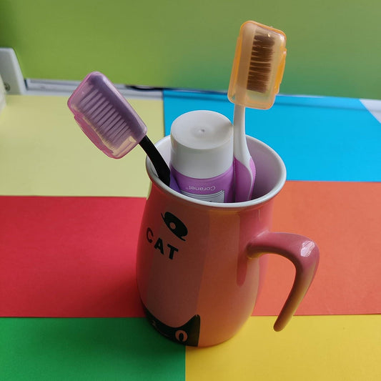 Toothbrush cap containers in purple and tan, shown in a cup with toothbrushes.