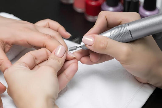 Electric nail drill in use: sanding bit attached while shaping a light-pink manicure